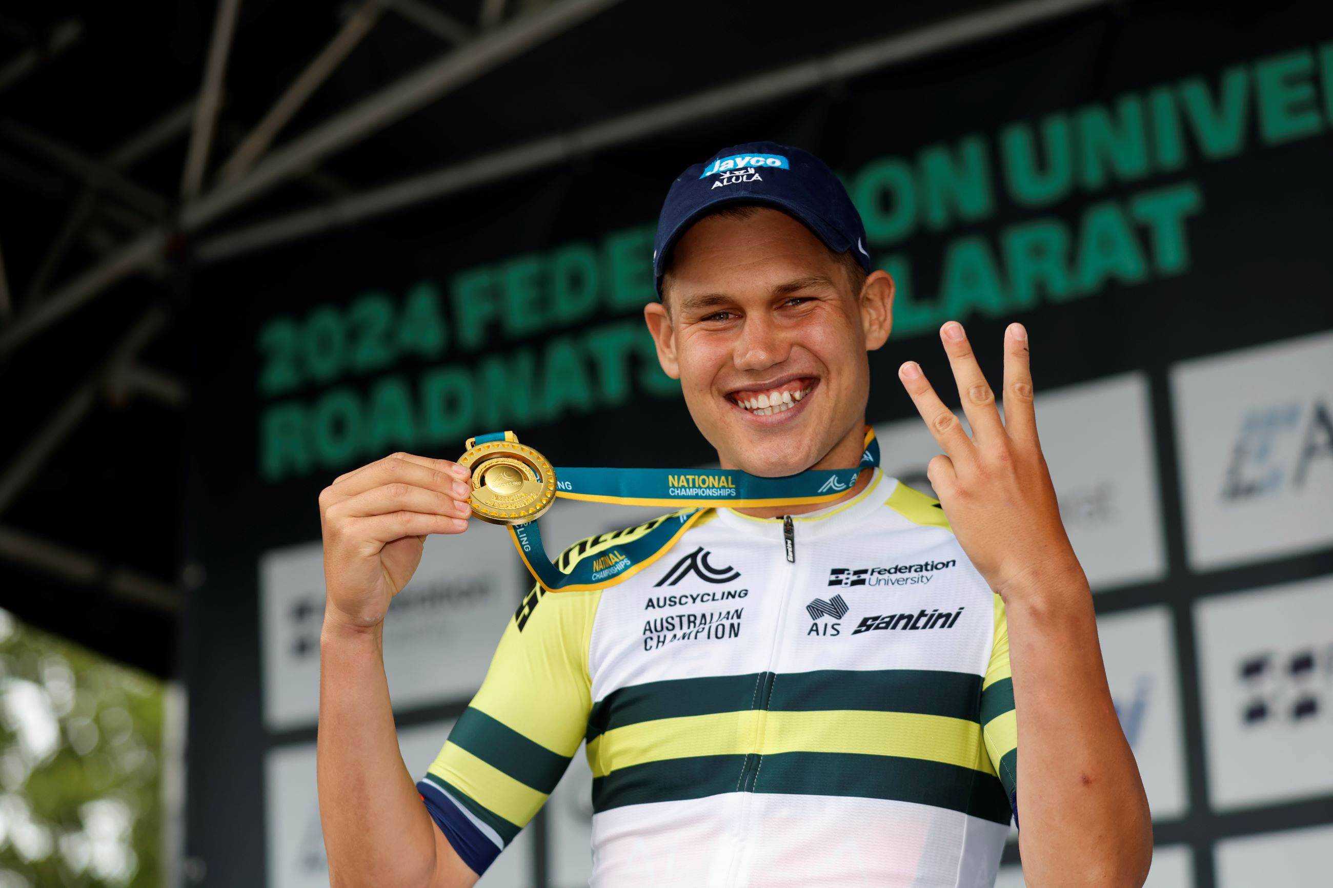 Lucas Plapp raises three fingers as he poses with the gold medal after winning his third consecutive Australian road race national championship in Ballarat, Victoria in January 2024